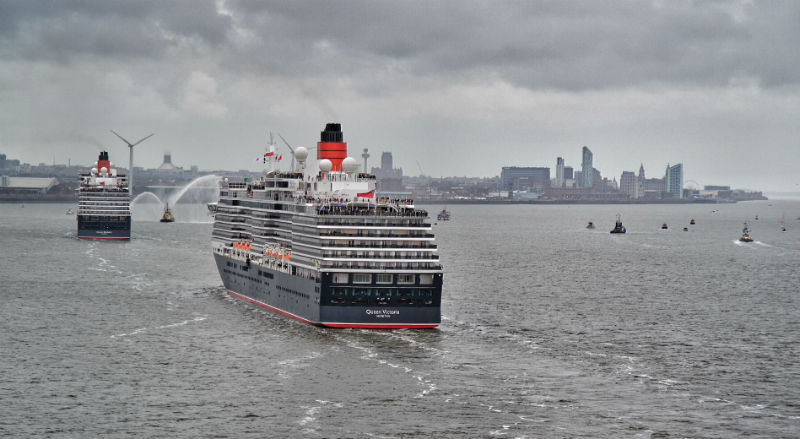 Cunard cruise liners Queen Victoria and Queen Elizabeth steam up the Mersey towards Liverpool's World Heritage waterfront, viewed from the flagship Queen Mary 2 bringing up the stern.